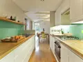 Cocina alargada con encimeras de madera, salpicadero verde turquesa y electrodomésticos integrados. Perfecta para distribuir el espacio.