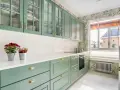 Encantadoras cocinas verdes vintage con armarios de cristal y detalles dorados. Flores rojas y naranjas adornan la encimera blanca.