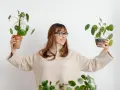 Mujer sonriente con gafas sostiene dos plantas altas de interior.