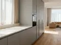Cocina moderna con armarios grises y una encimera de mármol clara. La luz del sol entra por las cortinas blancas, iluminando el espacio.