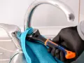 Mano enguantada usa llave inglesa para cambiar grifo cocina. Toalla azul protege el cromo.