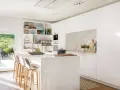 Cocina blanca moderna con isla central, estanterías abiertas y vistas al jardín. Ideas para decorar pared cocina blanca con estilo minimalista.