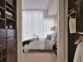 Dormitorio con vestidor integrado. Un espacio organizado con estanterías oscuras y cajones, que da paso a una cama acogedora y un armario con ropa colgada.