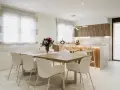 Elegantes cocinas abiertas al salón con barra, mesa de comedor y sillas blancas.