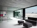 Interior moderno con sofá negro, sillones y una gran pared de cristal que da a un paisaje nevado y un coche descapotable.