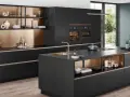Elegantes cocinas pequeñas con isla central negra, gabinetes dorados y electrodomésticos integrados.