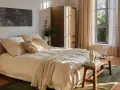 Habitación serena con cama beige, armario de madera y ventana con cortinas. Ideas decoracion habitacion: arte abstracto, plantas y luz natural.