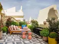 Sofá y taburetes coloridos en una terraza con fuente, ideal para decoracion terrazas pequeñas. Plantas y flores adornan este oasis urbano.