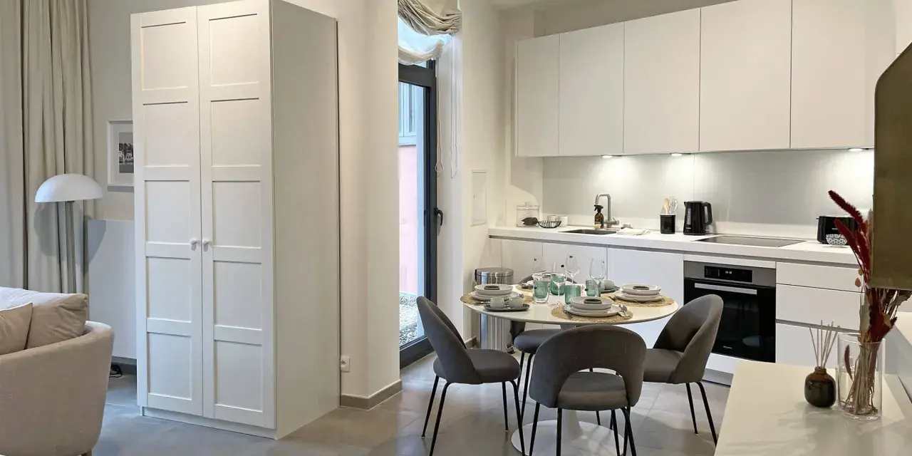 Acogedor cocina salón comedor de 30 m2 con muebles blancos, mesa redonda y sofá.