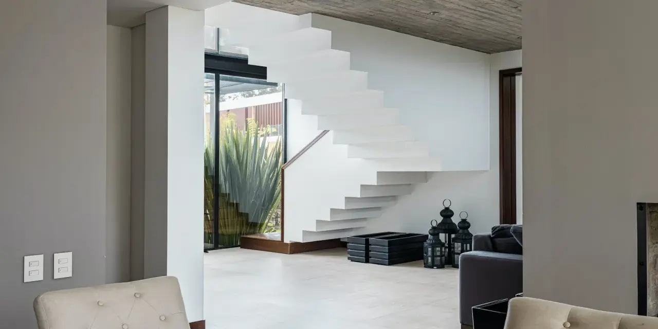 Moderna escalera blanca con un diseño flotante. El **rellano escalera decoracion descansillo escalera** se realza con linternas negras y maceteros.