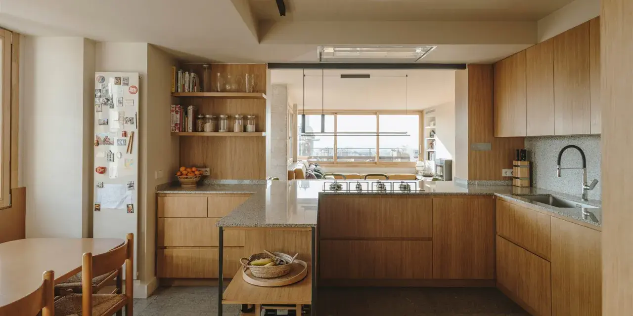 Cocinas color madera con encimeras de granito, electrodomésticos integrados y una isla central. Un comedor adyacente con mesa y sillas de madera.