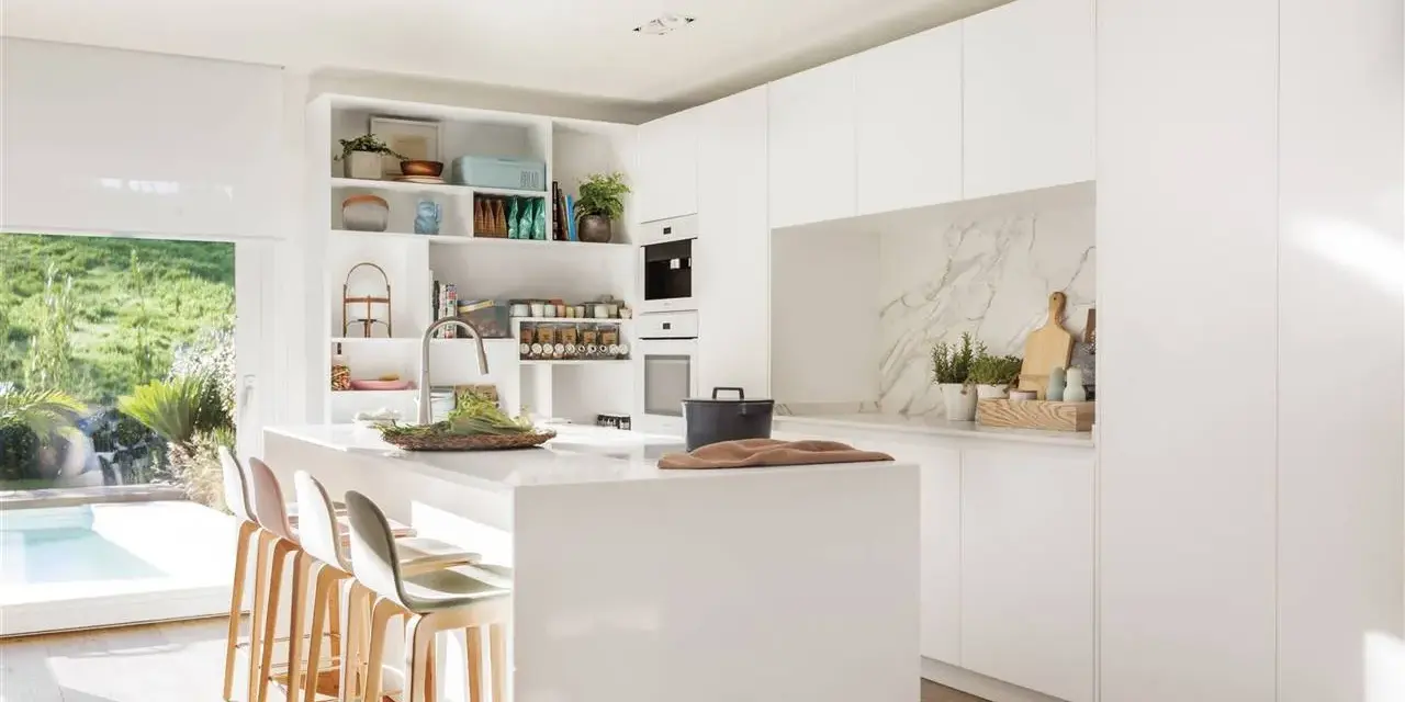 Cocina blanca moderna con isla central, estanterías abiertas y vistas al jardín. Ideas para decorar pared cocina blanca con estilo minimalista.