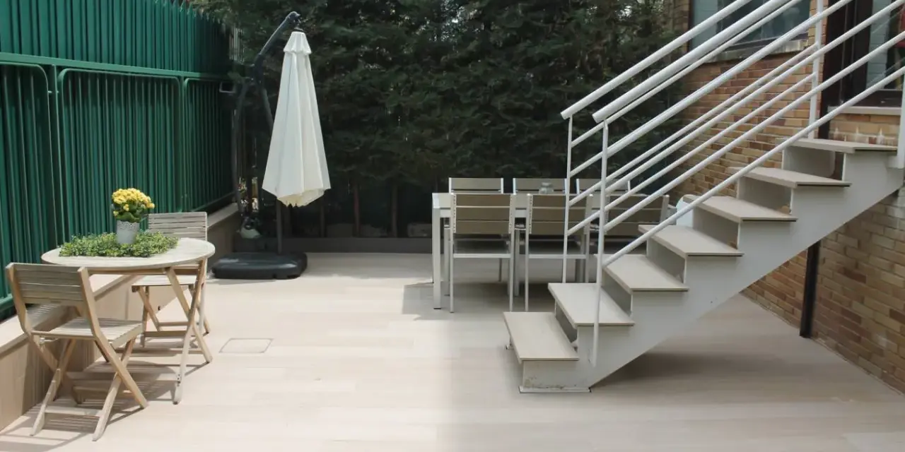 Escaleras exteriores casas de campo, con mesa y sillas de madera, sombrilla y valla verde.