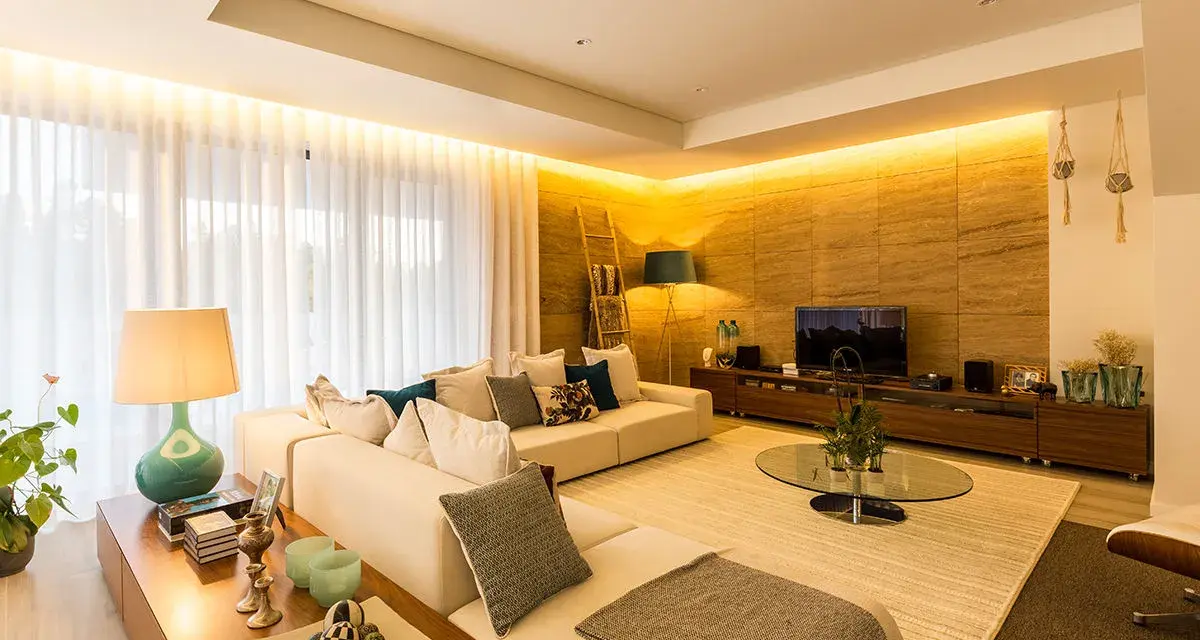 Salón moderno con sofá blanco, mesa de centro de cristal y **iluminación indirecta** cálida que realza la pared de piedra.