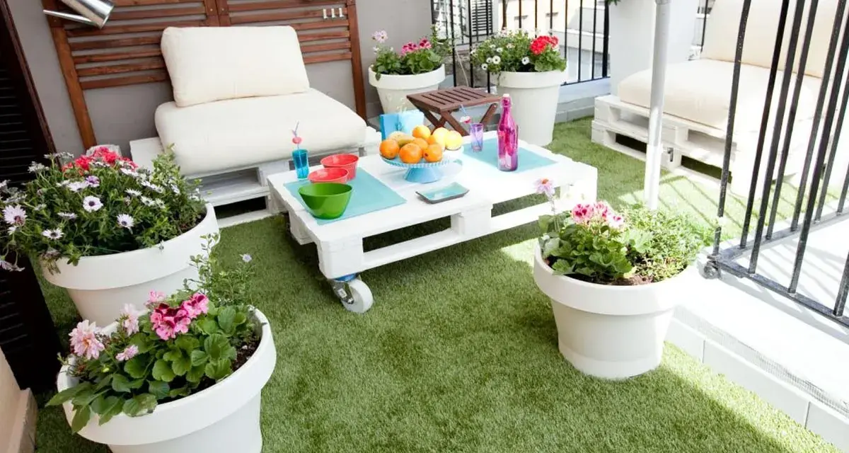 Balcón acogedor con césped artificial, muebles de palets y macetas con flores. ¡Ideas para terrazas con césped artificial!
