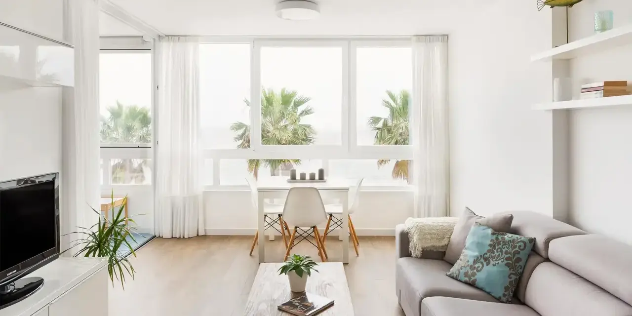 Acogedor salón nórdico rústico con sofá gris, mesa de centro de madera y vistas a palmeras.