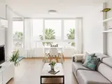 Acogedor salón nórdico rústico con sofá gris, mesa de centro de madera y vistas a palmeras.