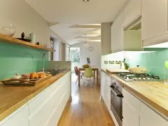 Cocina alargada con encimeras de madera, salpicadero verde turquesa y electrodomésticos integrados. Perfecta para distribuir el espacio.