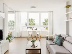 Acogedor salón nórdico rústico con sofá gris, mesa de centro de madera y vistas a palmeras.