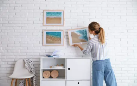 Mujer colocando cuadros de playa en pared de ladrillo blanco. Ideas para como combinar cuadros en la pared.