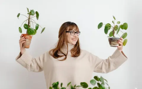 Mujer sonriente con gafas sostiene dos plantas altas de interior.