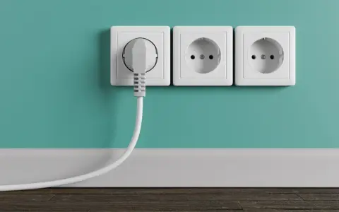 Tres enchufes blancos en una pared turquesa, uno con un enchufe gris conectado. La altura de los enchufes en la cocina es estándar.