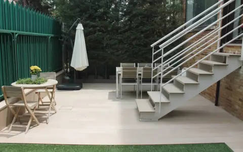 Escaleras exteriores casas de campo, con mesa y sillas de madera, sombrilla y valla verde.
