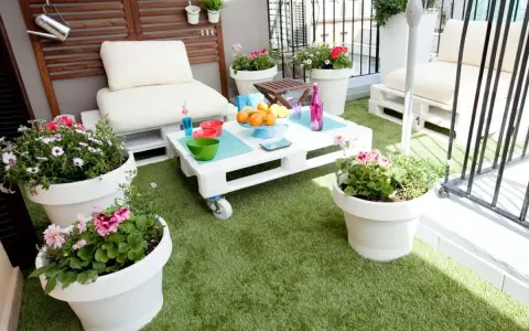 Balcón acogedor con césped artificial, muebles de palets y macetas con flores. ¡Ideas para terrazas con césped artificial!
