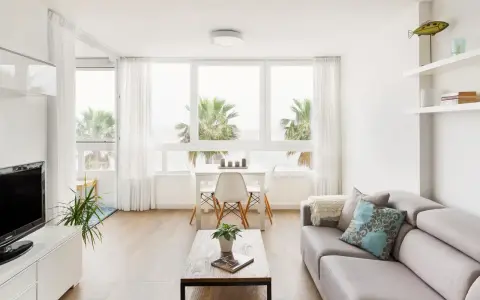 Acogedor salón nórdico rústico con sofá gris, mesa de centro de madera y vistas a palmeras.