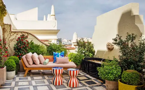 Sofá y taburetes coloridos en una terraza con fuente, ideal para decoracion terrazas pequeñas. Plantas y flores adornan este oasis urbano.