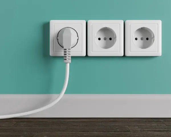Tres enchufes blancos en una pared turquesa, uno con un enchufe gris conectado. La altura de los enchufes en la cocina es estándar.