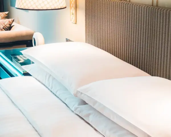 Cama de hotel con almohadas blancas y cabecero de mimbre. Una guía para saber como elegir un colchon.