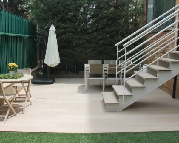 Escaleras exteriores casas de campo, con mesa y sillas de madera, sombrilla y valla verde.