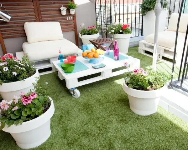 Balcón acogedor con césped artificial, muebles de palets y macetas con flores. ¡Ideas para terrazas con césped artificial!