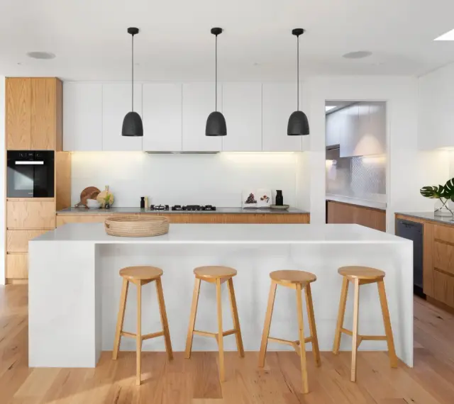 Moderna cocina blanca y madera con isla central, taburetes de madera y escaleras de diseño.