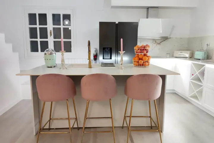 Elegantes cocinas con isla, tres taburetes rosas y dorados invitan a disfrutar.