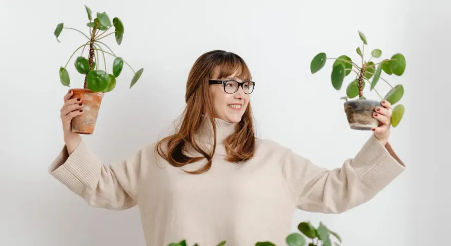 Mujer sonriente con gafas sostiene dos plantas altas de interior.