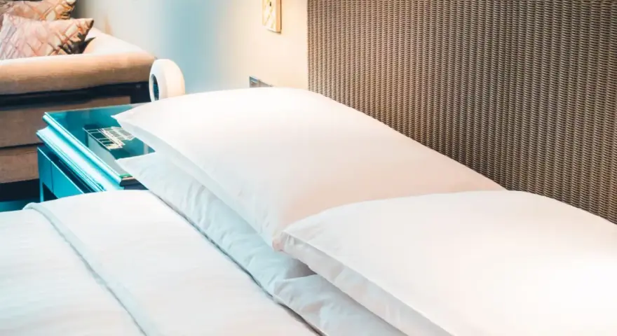 Cama de hotel con almohadas blancas y cabecero de mimbre. Una guía para saber como elegir un colchon.
