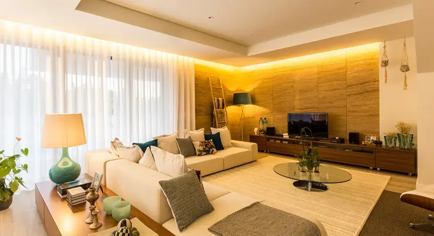 Salón moderno con sofá blanco, mesa de centro de cristal y **iluminación indirecta** cálida que realza la pared de piedra.