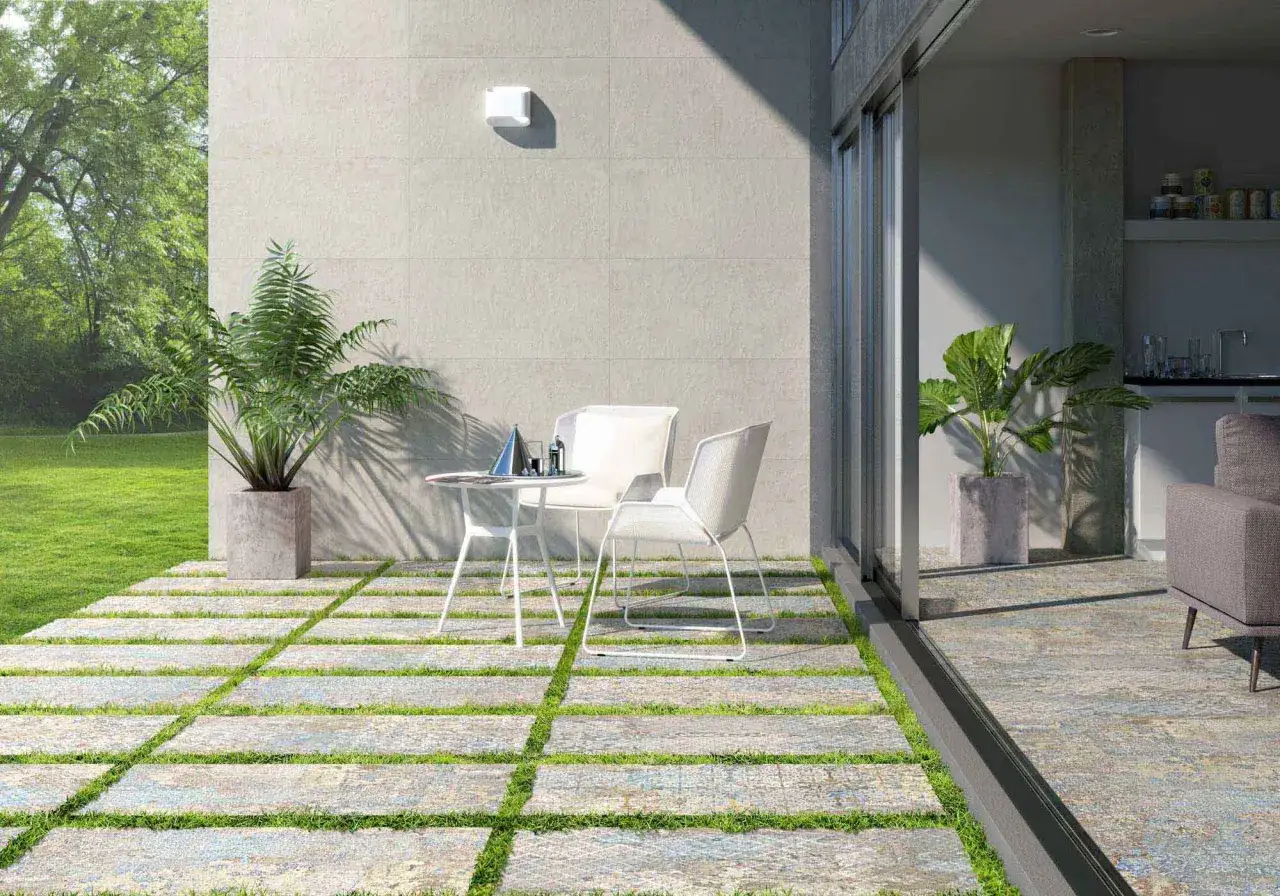 Modernos suelos para patios interiores con un dise&ntilde;o de baldosas y c&eacute;sped. Una mesa y sillas blancas invitan a relajarse al aire libre.