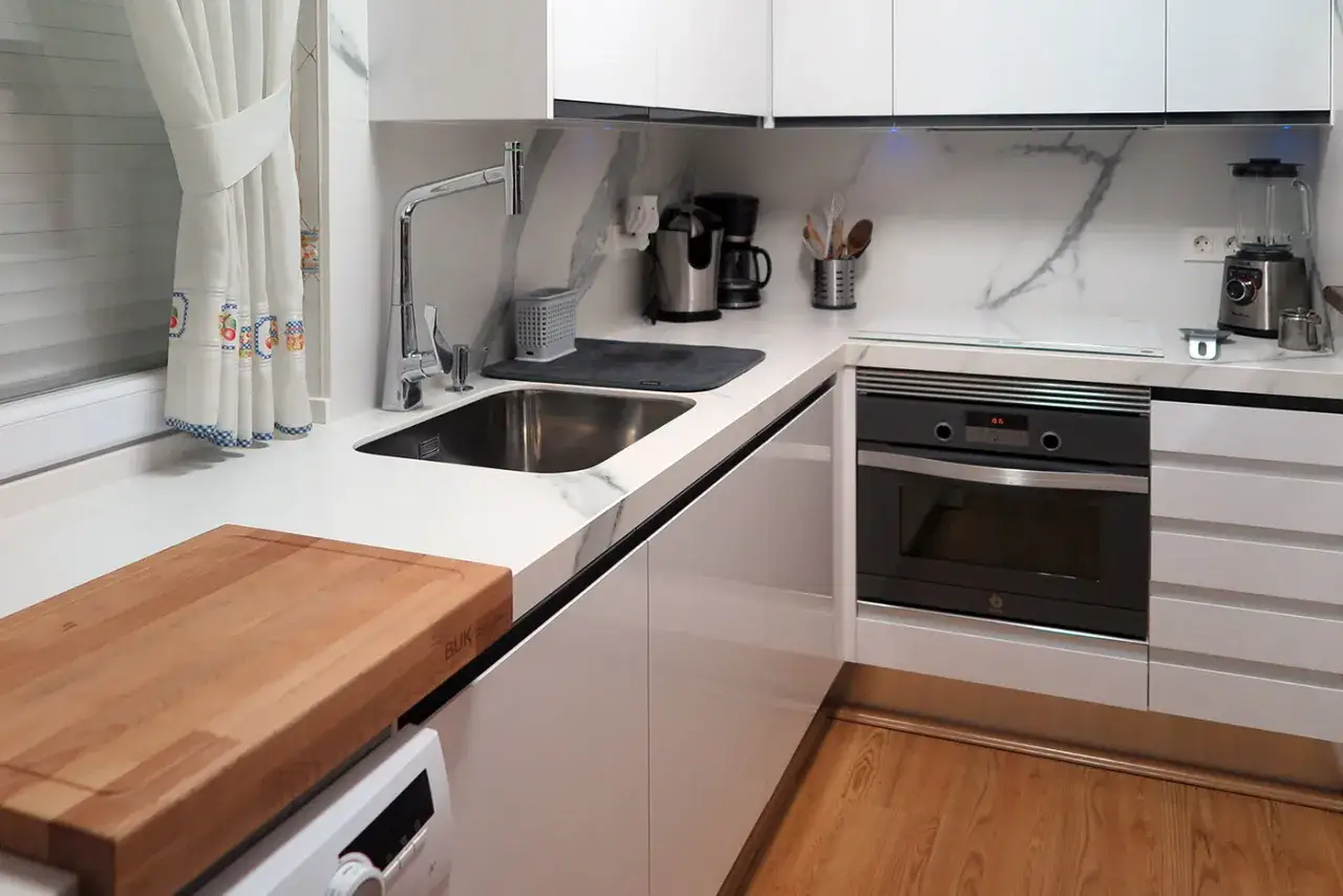Cocina moderna y funcional, lista para reformar. Encimera blanca, fregadero, horno y electrodomésticos.