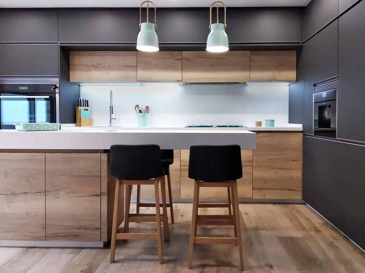Cocinas pequeñas con isla, modernas y funcionales, con encimera blanca, taburetes negros y armarios de madera.