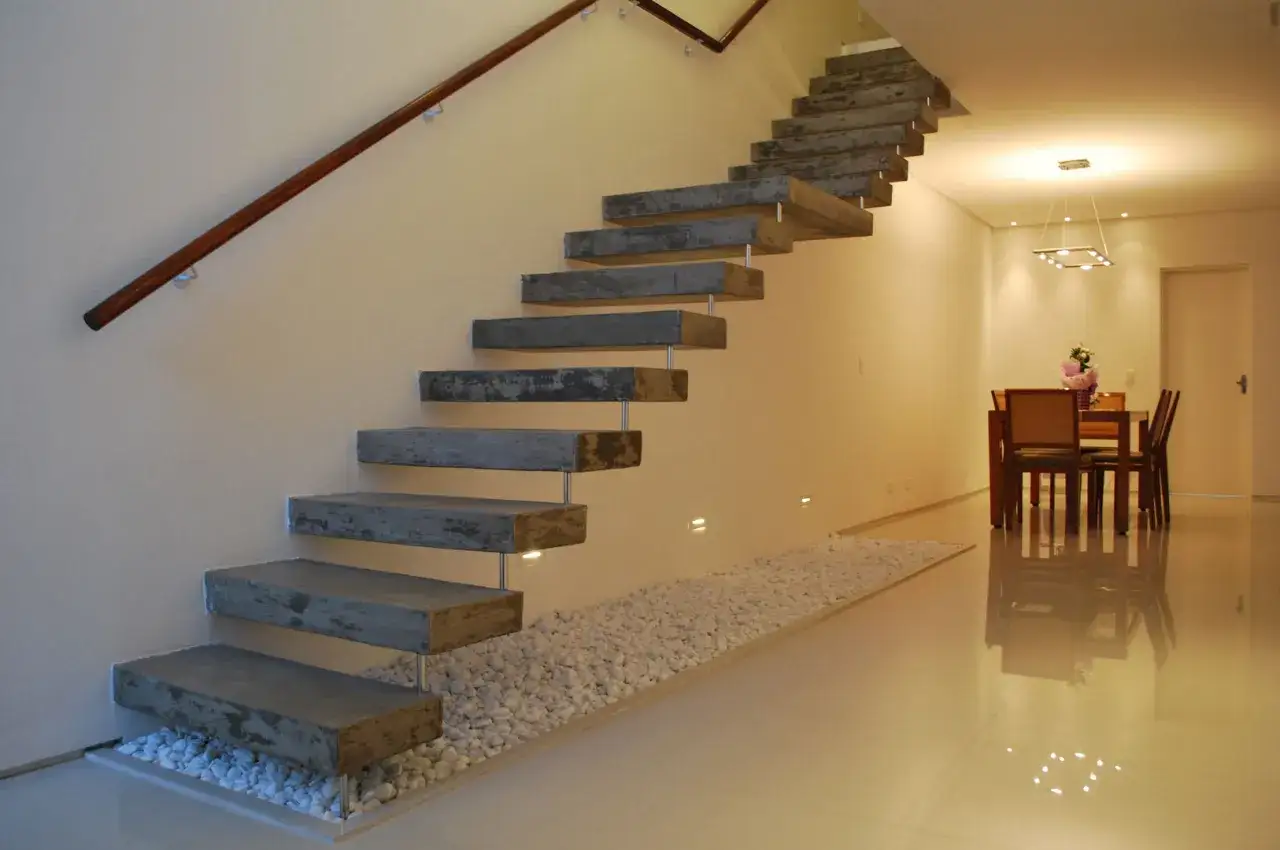 Escaleras de interior de obra con pelda&ntilde;os de hormig&oacute;n flotantes, barandilla de madera y guijarros blancos.