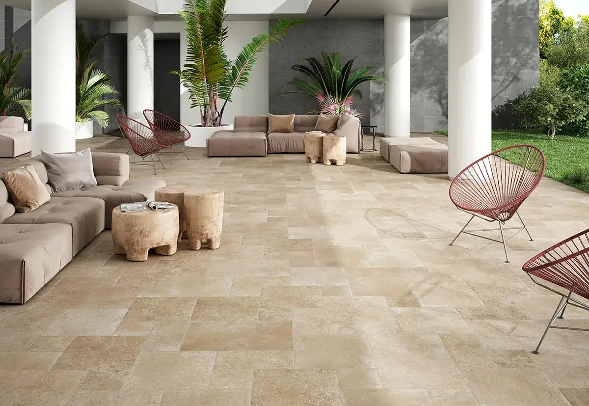 Amplia terraza exterior con suelo de baldosas de piedra natural, sof&aacute;s modulares, sillas rojas y vegetaci&oacute;n exuberante.