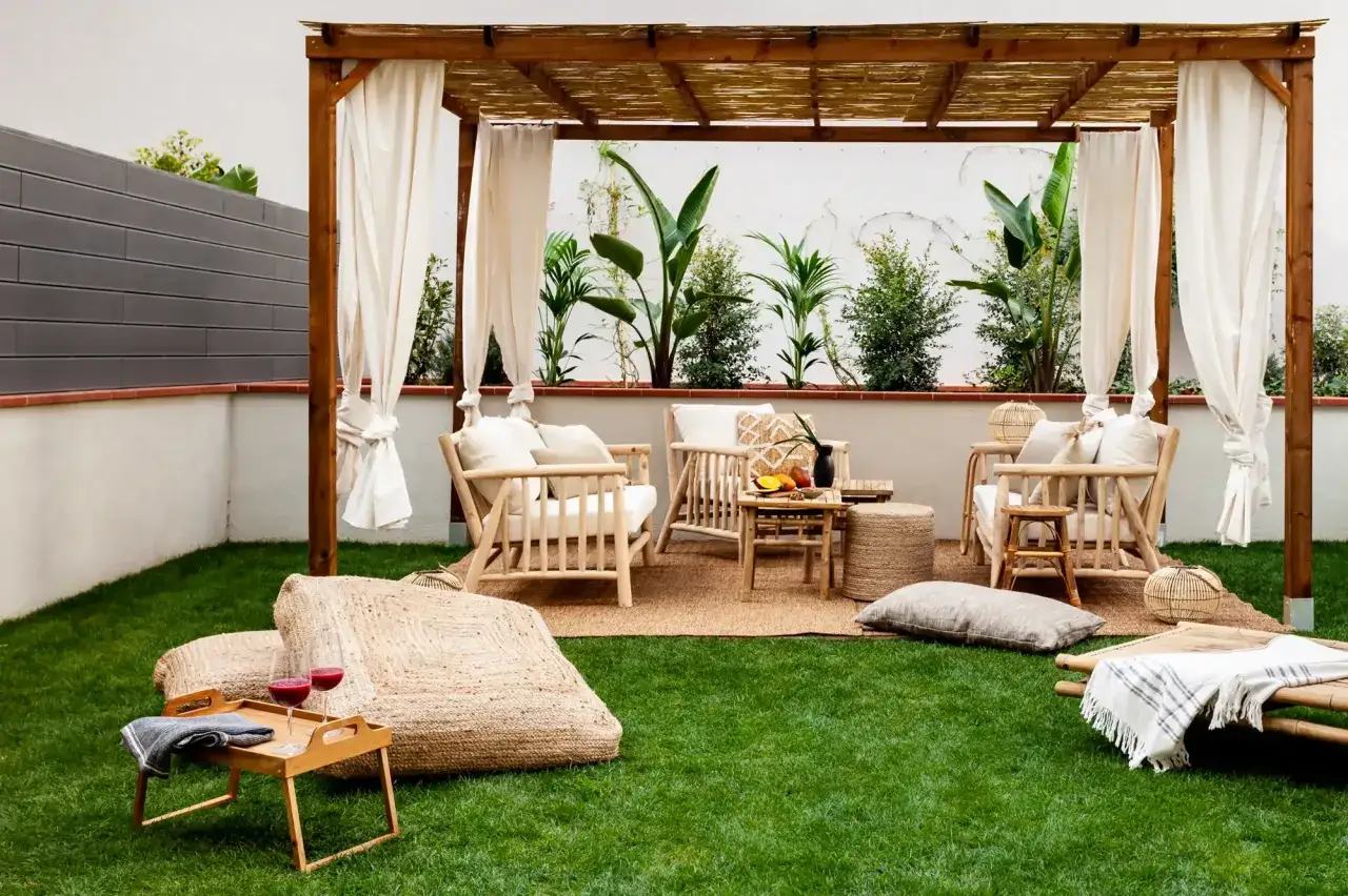 Ideas para terrazas con c&eacute;sped artificial: un rinc&oacute;n acogedor bajo p&eacute;rgola de bamb&uacute;, con muebles de madera clara y cojines.