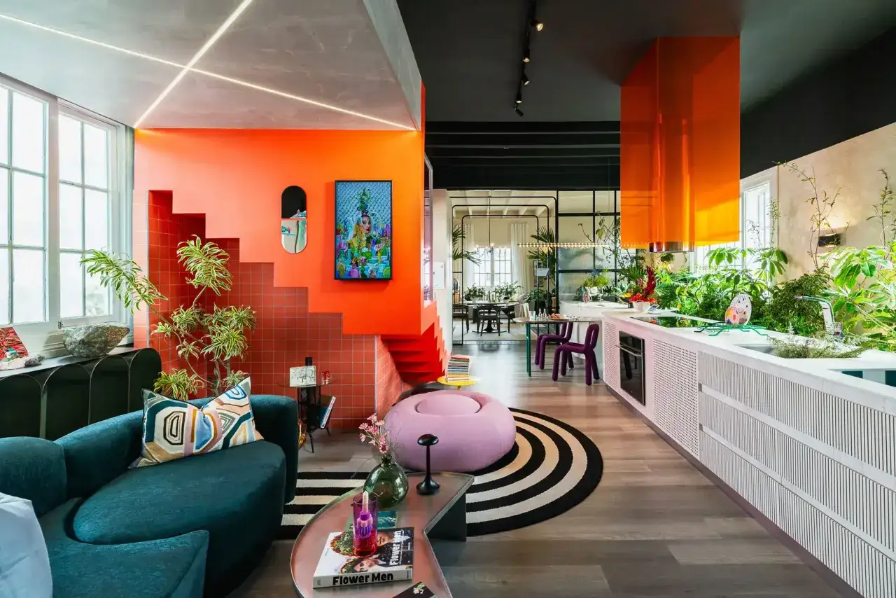 Un espacio vibrante con dopamine decor: sof&aacute; verde, escaleras naranjas, plantas exuberantes y una campana de cocina naranja brillante.