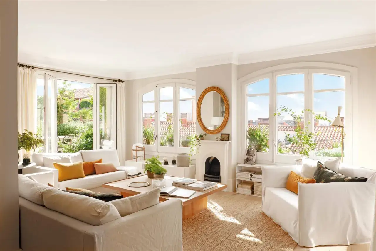 Acogedora decoracion salon con sofás blancos, mesa de madera y grandes ventanales que dan a un jardín.