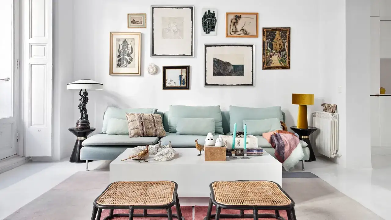 Un sof&aacute; azul claro con cojines decorativos y una colecci&oacute;n de arte en la pared. Ideas de que poner detras del sofa para un estilo ecl&eacute;ctico.
