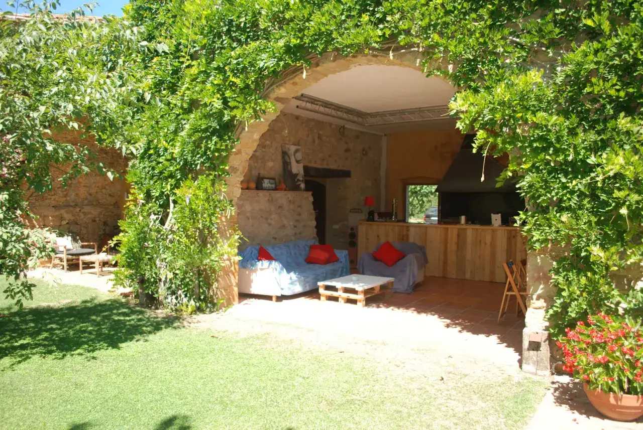 Un patio acogedor con sofás y una barra de madera, cubierto por una exuberante madreselva planta.