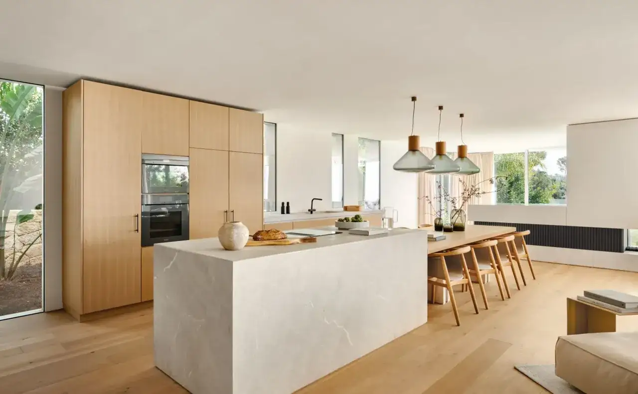 Cocinas modernas con isla de cuarzo, gabinetes de madera clara y electrodomésticos integrados. Mesa de comedor de madera con sillas de diseño.